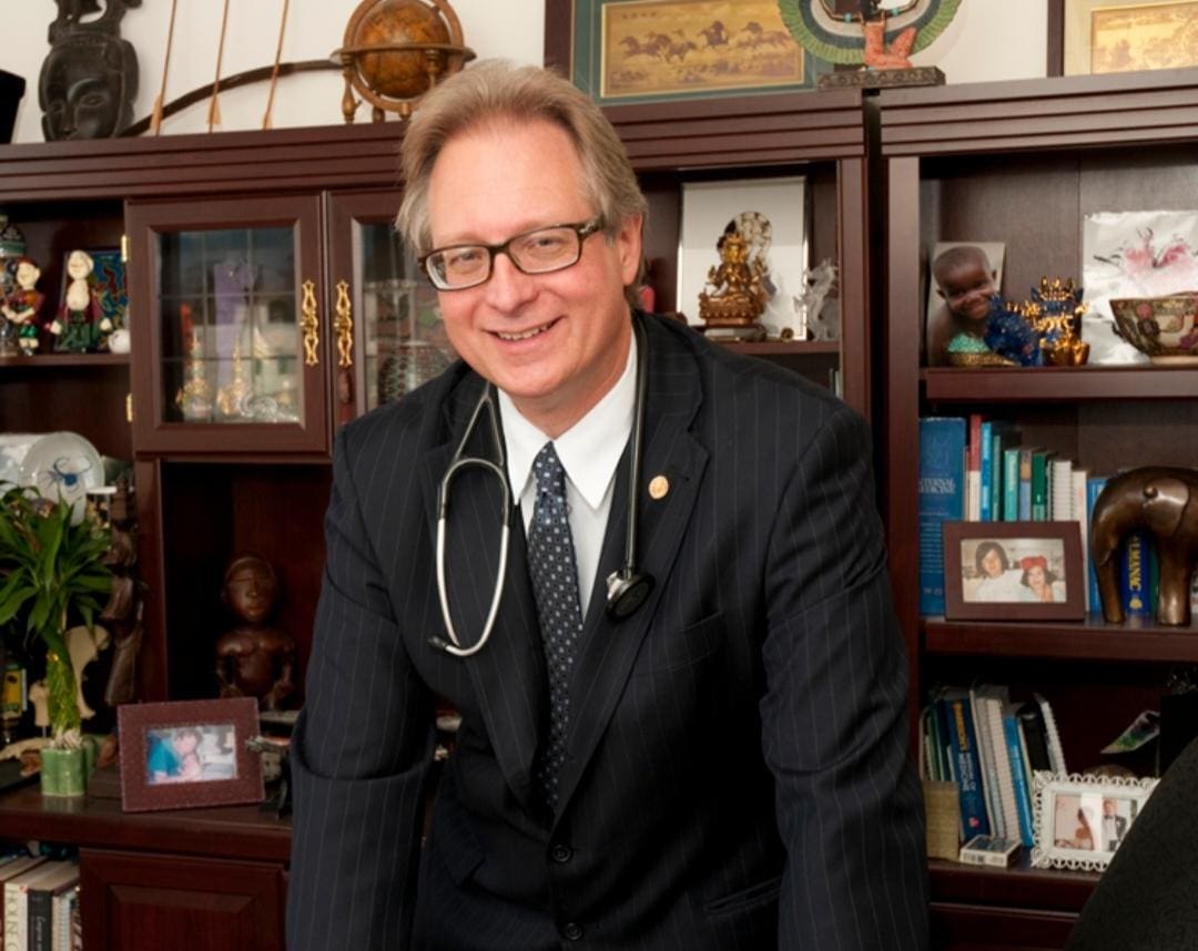 A man in suit and stethoscope standing next to bookcase.